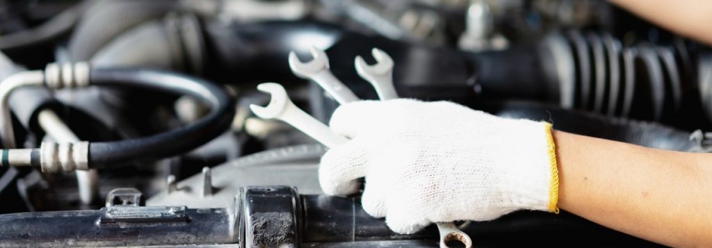 Mechanic holding wrenches by a car engine