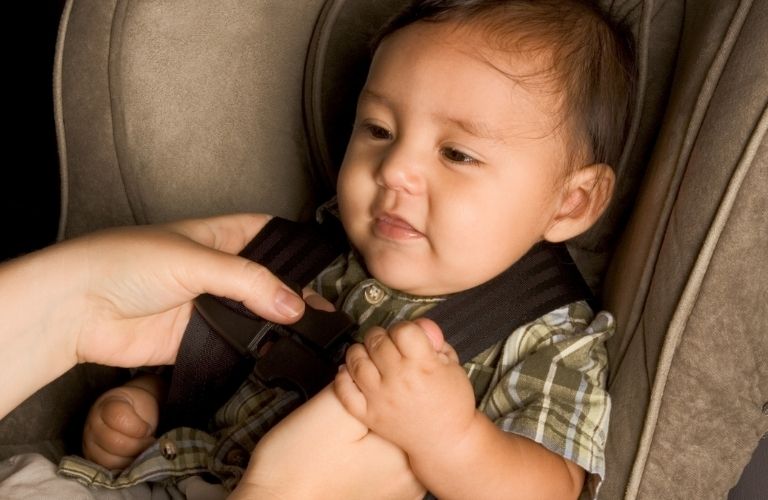 An infant smiling out of joy and comfort while its caretaker straps the child safety seat on