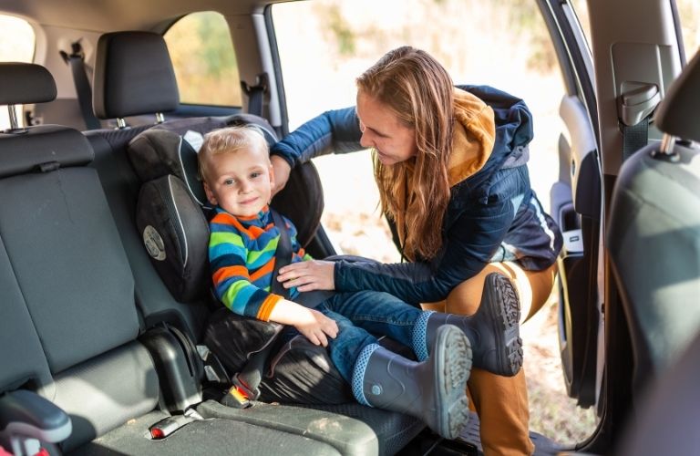 A young woman places a child inside a car