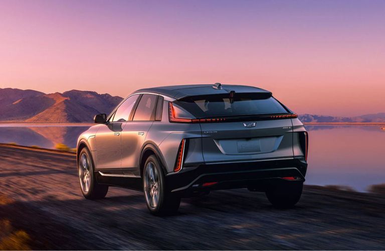 Rear side view of a 2023 Cadillac Lyriq electric crossover SUV parked in front of a lake