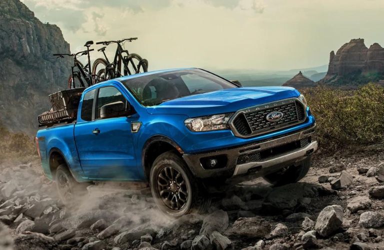 A blue 2023 Ford Ranger carrying cycles on rocky terrain.