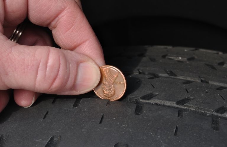 a hand checking the tread of a tire using a penny