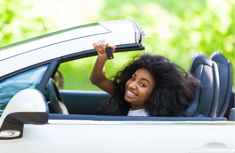 a young girl smiling while holding a car key in driver's seat